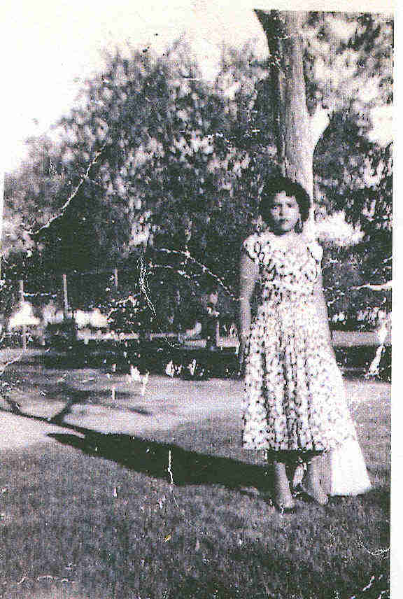 A young Lula Martinez, poses by a tree in a patterned dress.