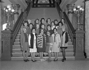 Nineteen women delegates stand in front of the grand staircase in the capitol rotunda.