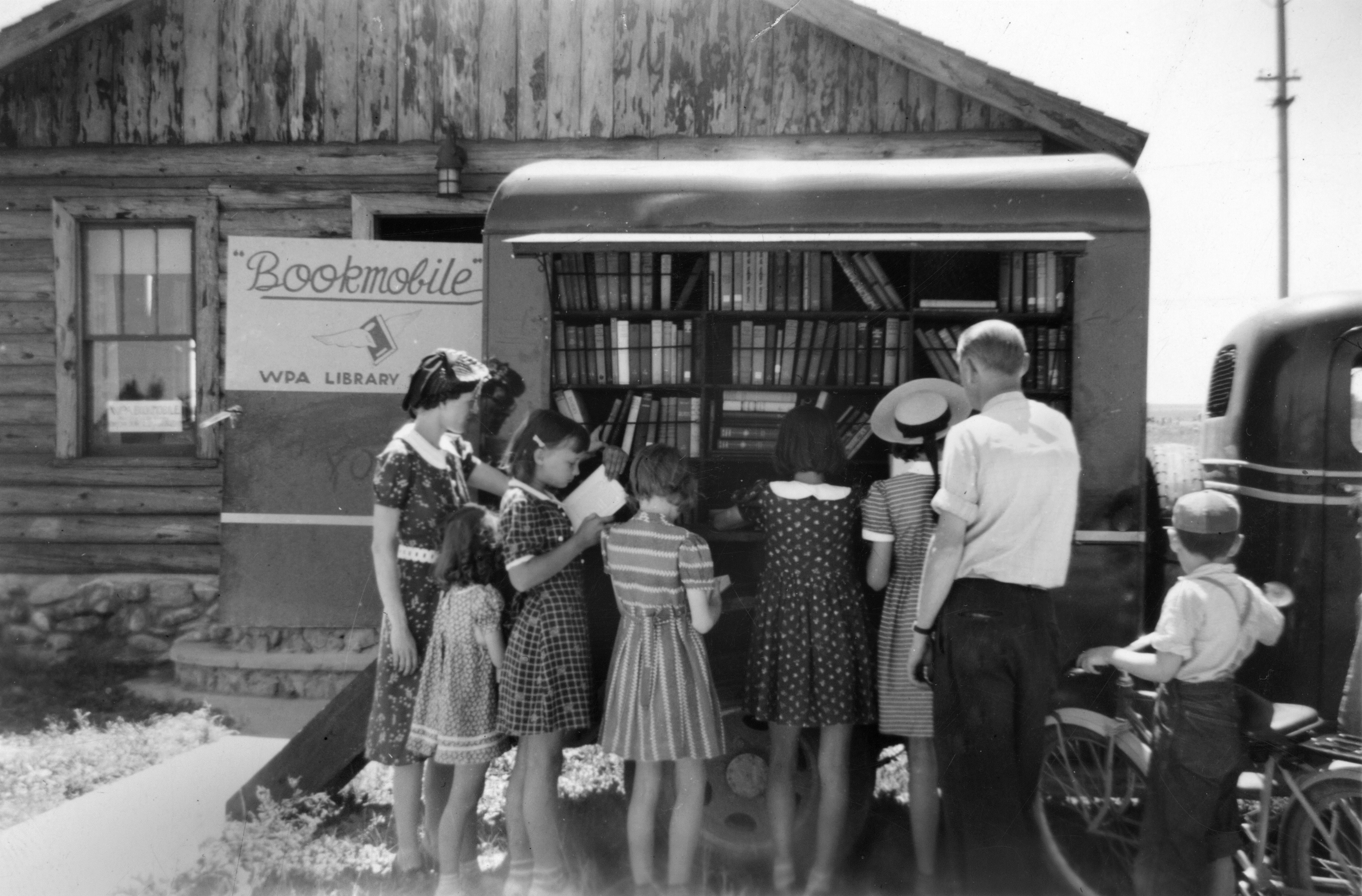 A group of young women gather around a Works Progress Administration (WPA) Bookmobile in Fairfield, Montana. A woman, man, and young boy are also present. Date unknown.
