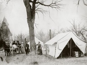 One of the first two women to serve as an allotment agent. Clarke is shown here standing next to the wagon. at the Otoe Agency in Oklahoma, circa 1891. The beautiful quilt on her bed hints at her effort to make camp life comfortable. MHS PHoto Archives 941-747