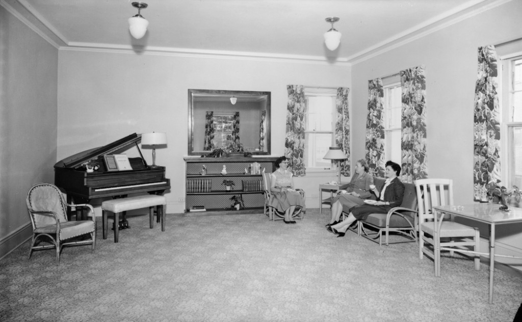 This 1957 photo shows the interior of the Helena YWCA. A piano sits in the corner. On the other side of the room, three women drink tea. 