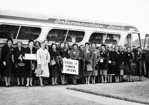 A large group of women holding a sign, League of Women Voters," stands in front o f an Intermountain Line bus.